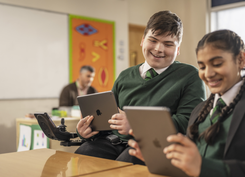 2 Students, One In A Wheelchair, Sharing Their Work On Their Ipad In The Classroom