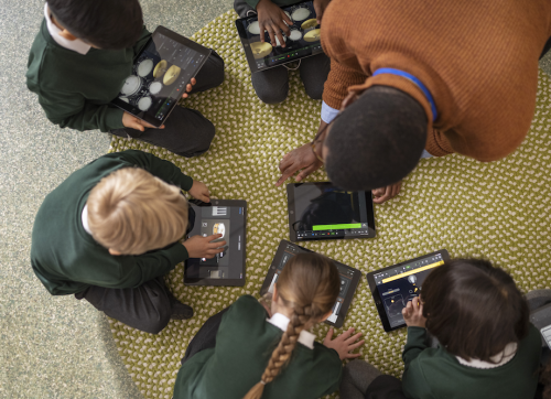 Students And Their Teacher Working On The Floor Creating Music On Ipad With Garage Band