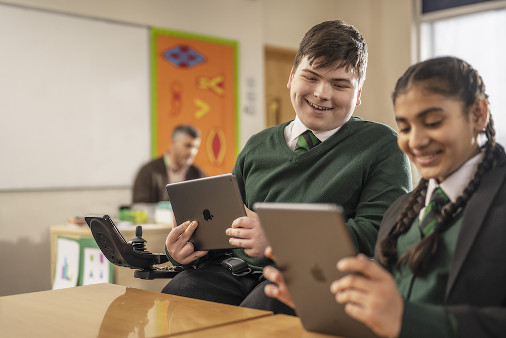a student in a wheelchair and a female student looking at an ipad in school